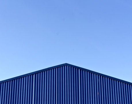 Blue modern warehouse roof against blue sky.