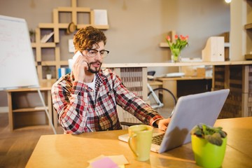 Graphic designer using laptop while talking on mobile phone