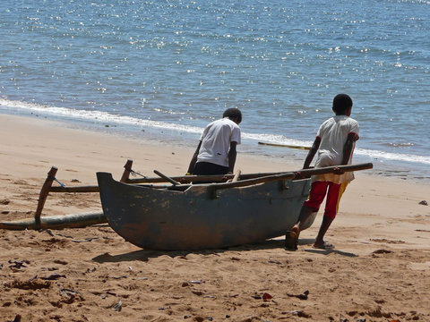 Deux enfants tirent une pirogue sur une plage afin de la mettre à l'eau et d'aller jouer sur la mer. Scène de vie de l'océan Indien. 