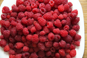 Fresh raspberries in a white plate on a wooden table