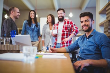Confident creative businessman with colleagues standing by table