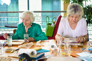 Two adorable senior women painting at table.