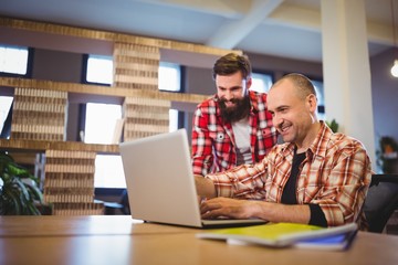 Male colleagues smiling while discussing over laptop 