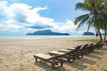 Beach chairs and coconut palm tree at the tropical beach. Pranburi, Thailand.
