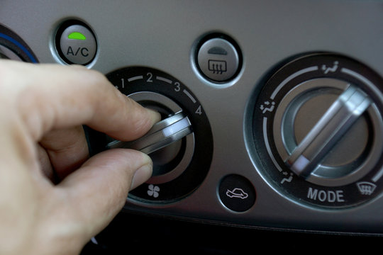 Left hand adjusting a fan level control knob of the car's air conditioning system.