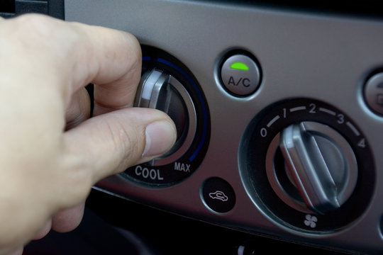 Left hand adjusting a temperature control knob of the car's air conditioning system.