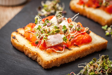 Grilled toasted bread with roasted tomatoes, feta cheese and radish sprouts.