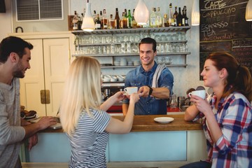 Handsome waiter serving coffee to customer with friends