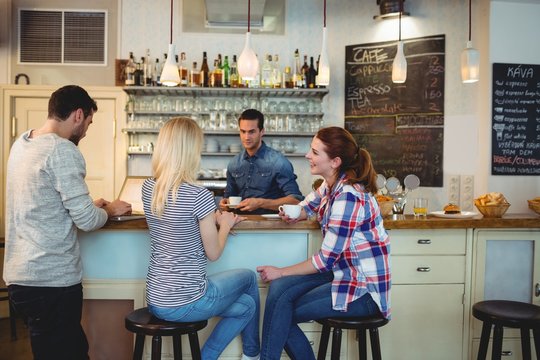 Waiter looking at female customers sitting at counter in cafe