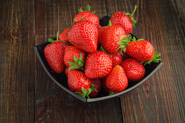 Strawberries with leaves in black plate. wooden background.