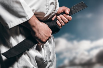 Composite image of fighter tightening karate belt - obrazy, fototapety, plakaty