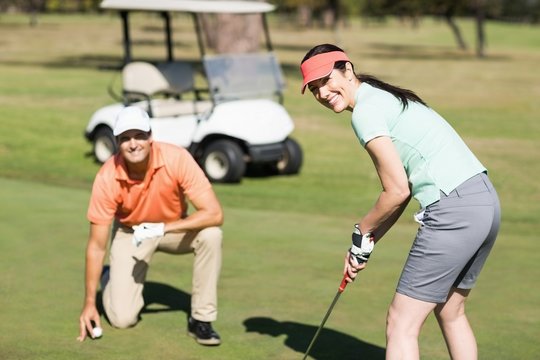 Portrait of smiling woman playing golf while standing by man 