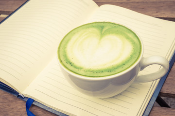 cup of green tea on the notebook and wood background