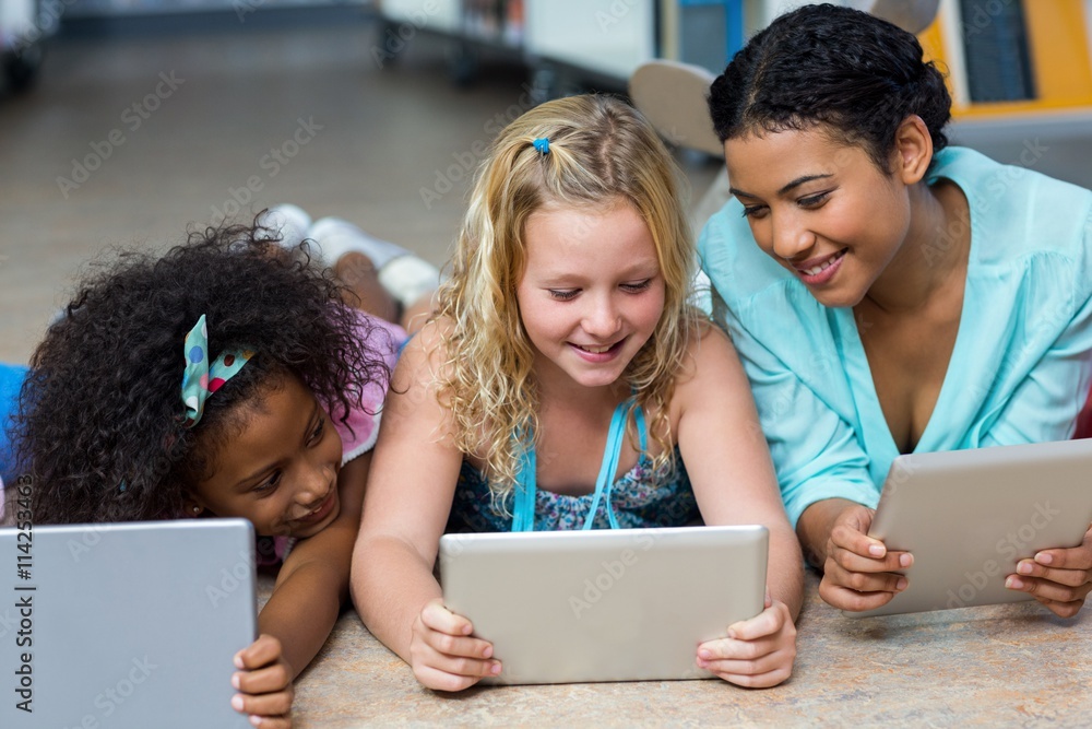 Wall mural Smiling teacher with girls using digital tablets