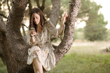Woman with Smartphone Sitting on a Pine Tree in a Park