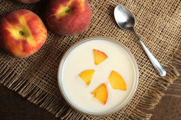 delicious and juicy peaches in a glass bowl with yogurt on a burlap on wooden background