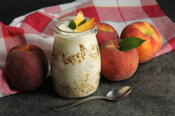 peach with a green leaf lying near the banks with the yoghurt and dessert spoon on the fabric on a dark background