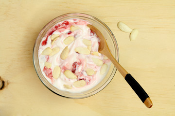 Bowl of strawberry yogurt with almonds and a wooden spoon.