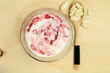 Bowl of strawberry yogurt with almonds in a wooden spoon.