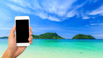 Hand hold smartphone on beautiful tropical beach and sea background