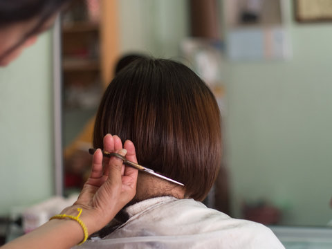 Hair stylist trimming short hair young asian woman.