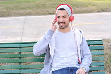 Young man listening to music with headphones sitting on park ben