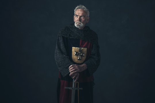 Senior knight in hauberk standing with sword.