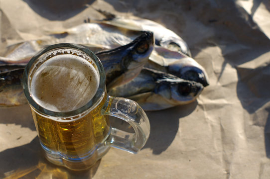 Glass of beer and salty fish (Pelecus cultratus) on gray crumpled paper, top view. Beer and snack to beer.