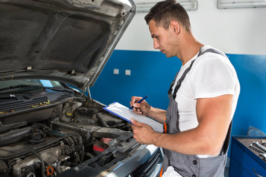 Mechanic man holding clipboard and check the car