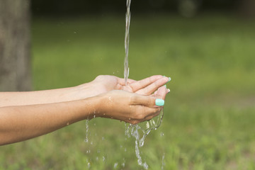 A stream of fresh clean water flowing to the hands of a girl with beautiful manicure