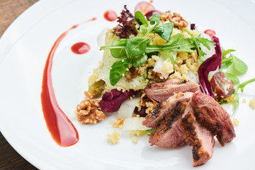 Salad of duck breast, daikon, grapes and couscous served on a white plate