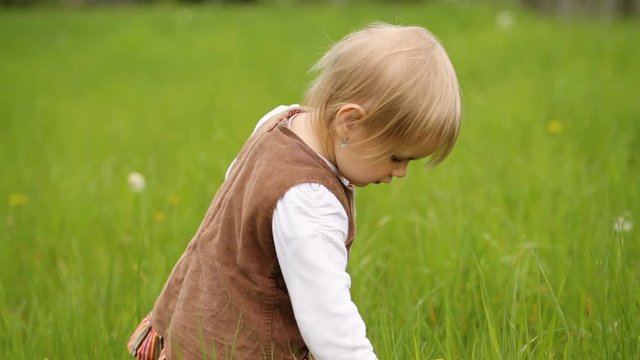 Adorable little girl in cute brown dress playing on the grass.