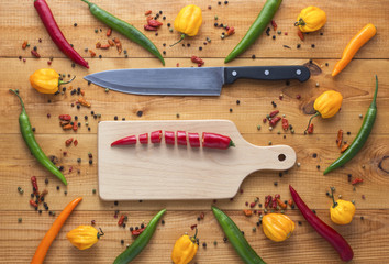 chopped cayenne chilli pepper on cutting board with knife and cayenne chili peppers, habanero peppers, pepperoncino peppers and color peppercorns on wooden table. Image with copyspace.
