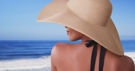Woman with big sunhat looking out over ocean on vacation
