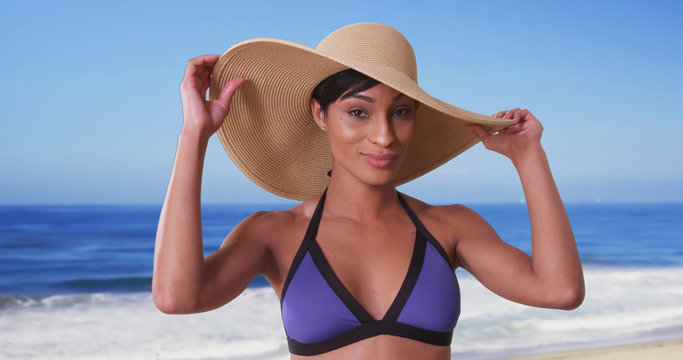 Beautiful black woman with sunhat on the beach enjoying the sun