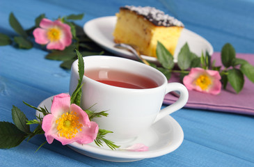 Cup of tea with cheesecake and wild rose flower on blue boards
