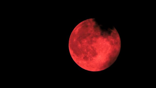 
Red moon moves across the night sky with dark clouds.