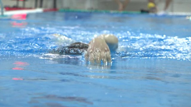 Young man swims in swimming pool towards the camera. Slow motion shot