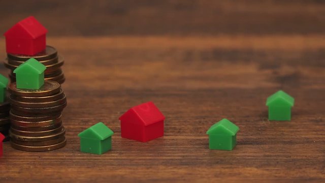 Real estate mortgage concept with small plastic house models on top of stacked coins, camera sliding across wooden desk