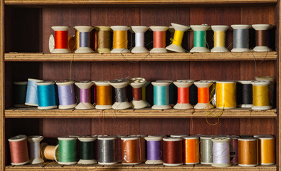 Old and colorful thread spools on wooden shelf.