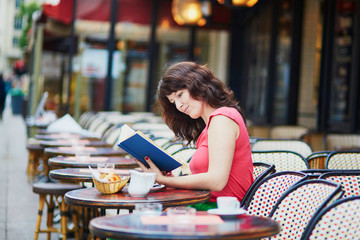 woman reading a book in traditional Parisian outdoor cafe, Paris, France
