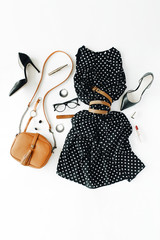flat lay feminini clothes and accessories collage with black dress, glasses, high heel shoes, purse, watch, mascara, lipstick, earrings on white background.