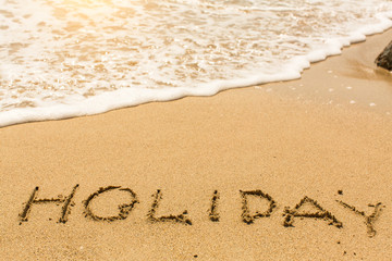 Holiday - word drawn on the sand beach with the soft wave.