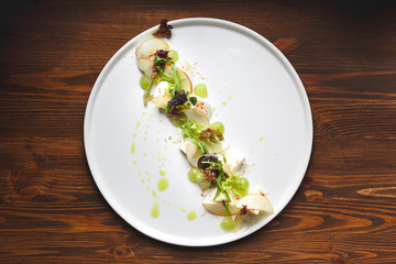 Salad is laid out diagonally on a large round dish, mozzarella, grapes, Apple, arugula and fresh Basil