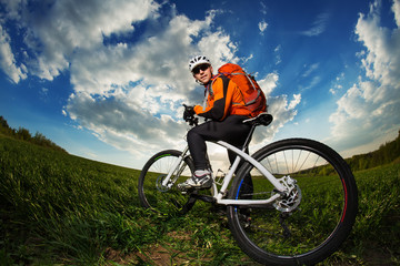 Young man riding on bicycle through deep grass with backpack