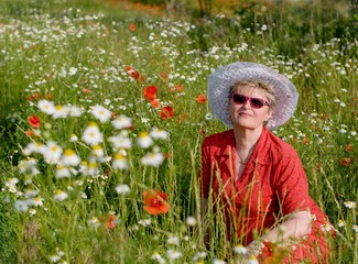 The woman with poppies and chamomile./The elderly woman sitting in a meadow with poppies and chamomiles.