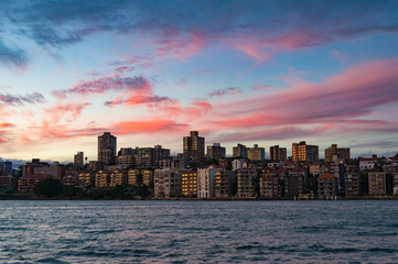 Fototapeta na wymiar Cityscape with dramatic colorful evening sky on the background. Modern buildings of Kirribilli suburb of North Sydney, Australia. Urban sunset landscape with space for text