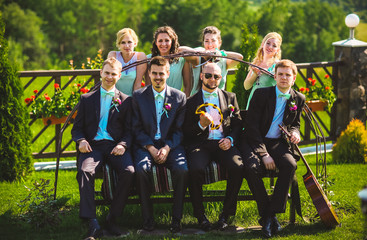 Bridesmaids and groomsmen of wedding couple posing in park.Sitting on the bench. Bridesmaids in...