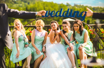 Bride with bridesmaids on the park on the wedding day sitting on the bench. Bridesmaids in same...