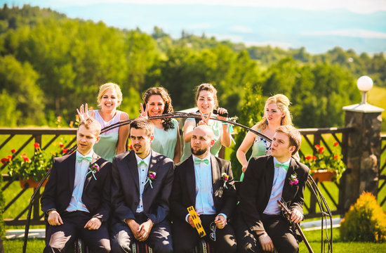 Bridesmaids and groomsmen of wedding couple posing in park.Sitting on the bench. Bridesmaids in same color dress.